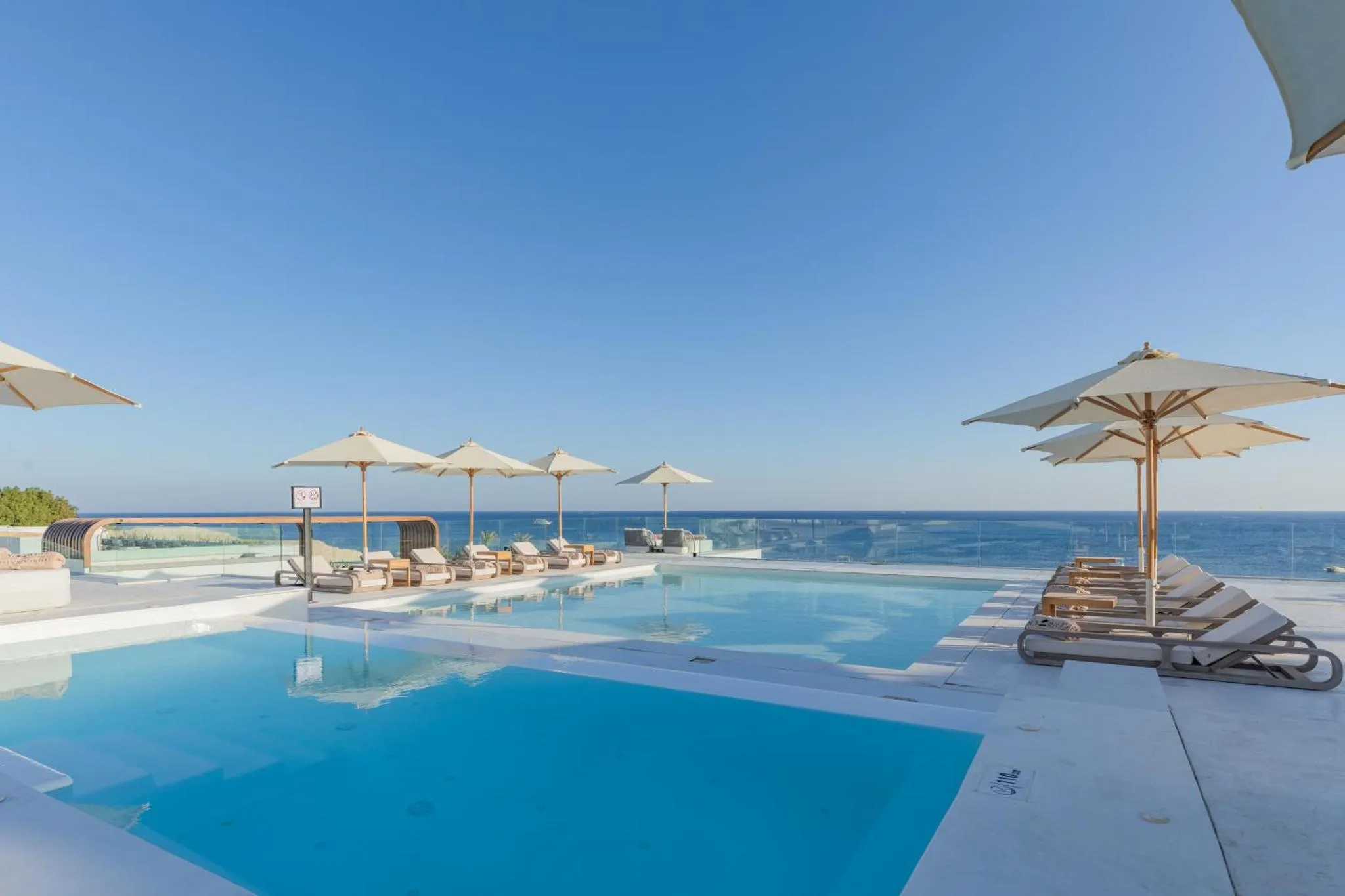 Terrasse avec transats et piscine à débordement donnant sur la mer.