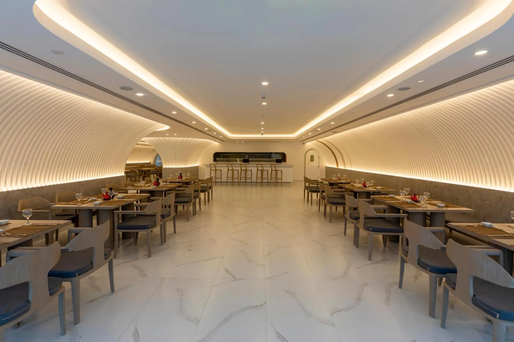 Une salle de restaurant lumineuse avec des tables dressées et un comptoir de bar.