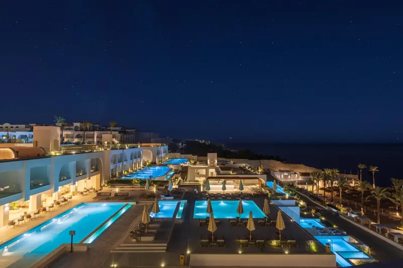 Vue nocturne sur des piscines illuminées d'un complexe hôtelier en bord de mer.