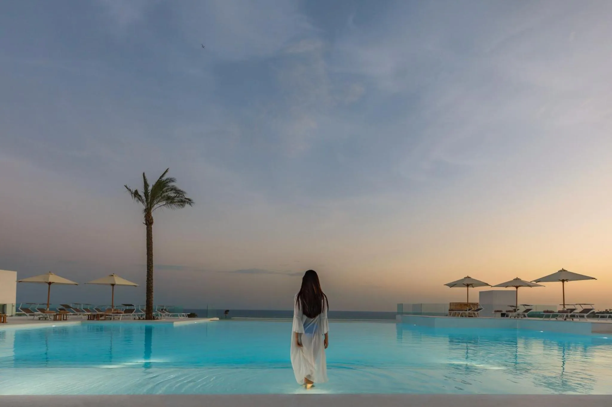Une femme se tient au bord d'une piscine à débordement face à la mer.