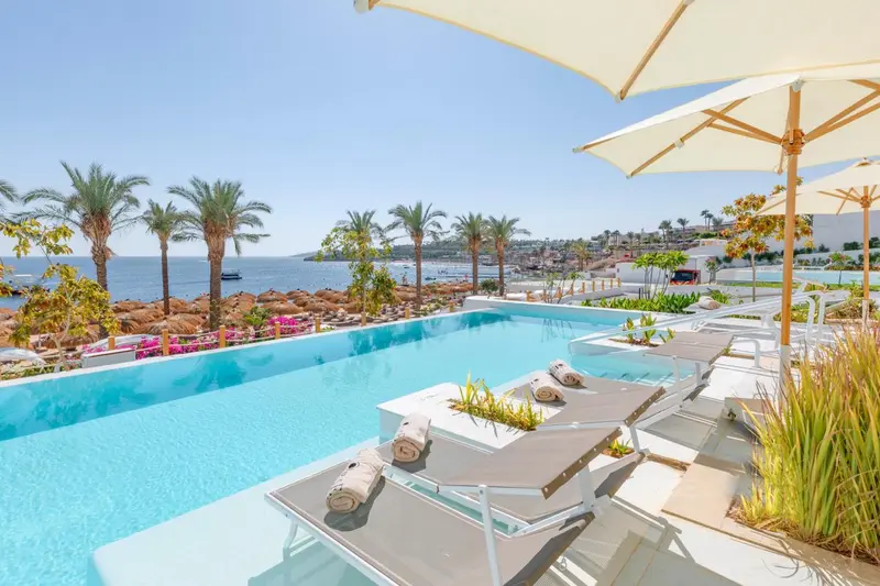 Transats et parasols bordent une piscine à débordement avec vue sur la mer.