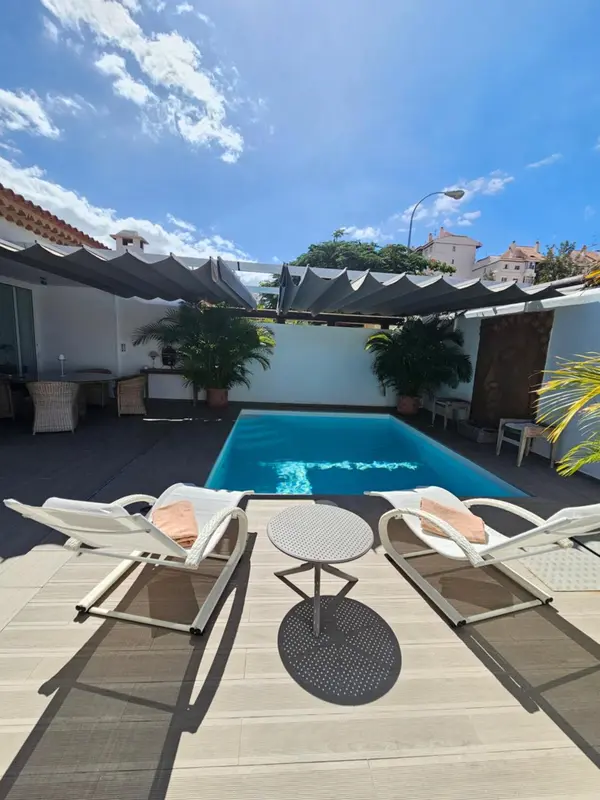 Transats blancs disposés autour d'une piscine rectangulaire sous des parasols gris.