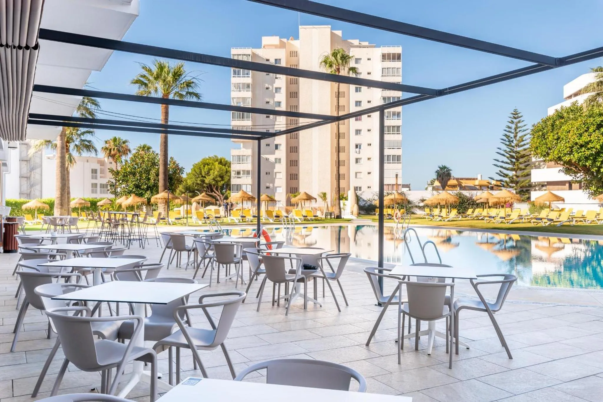 Terrasse ombragée avec tables et chaises près d'une piscine.