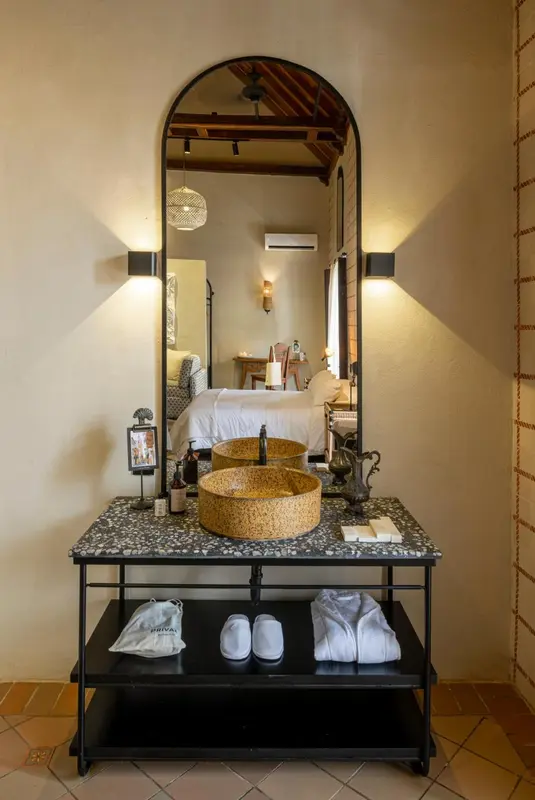 Une salle de bain lumineuse avec un lavabo en pierre et un miroir en arc de cercle.