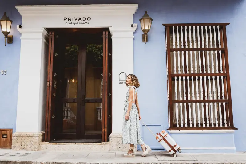 Une femme tire une valise devant l'entrée d'un bâtiment bleu.