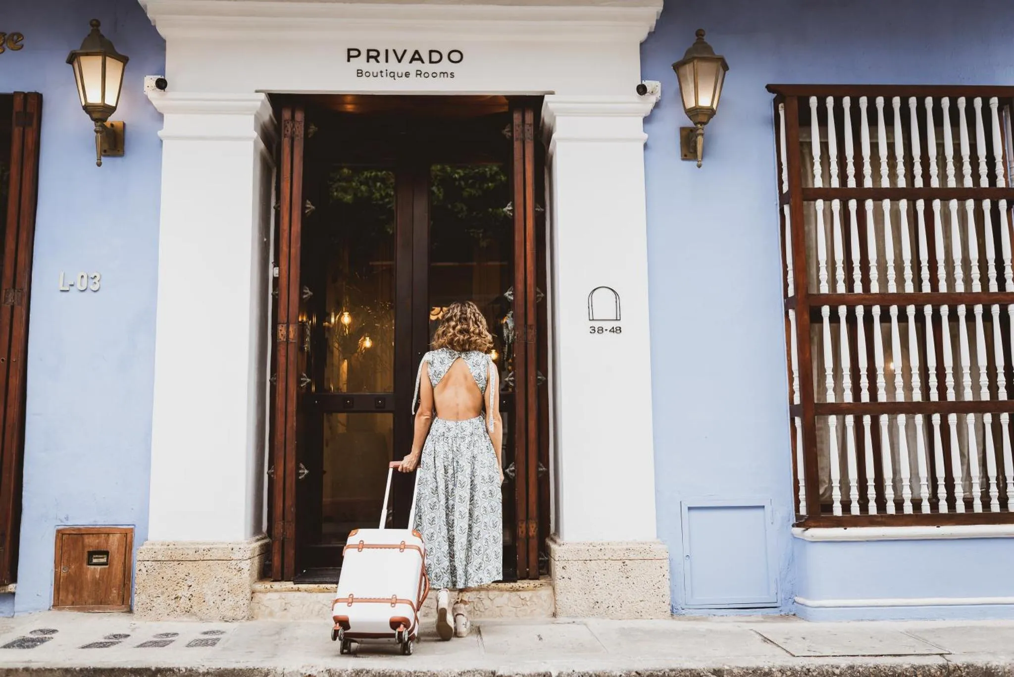 Une femme tire une valise devant l'entrée d'un bâtiment bleu.
