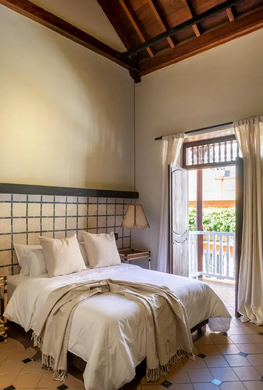 Une chambre lumineuse avec un lit recouvert de draps blancs et une ouverture sur une terrasse.