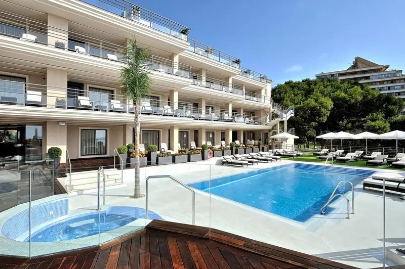Vue d'un bâtiment blanc avec des balcons donnant sur une piscine et un jardin.