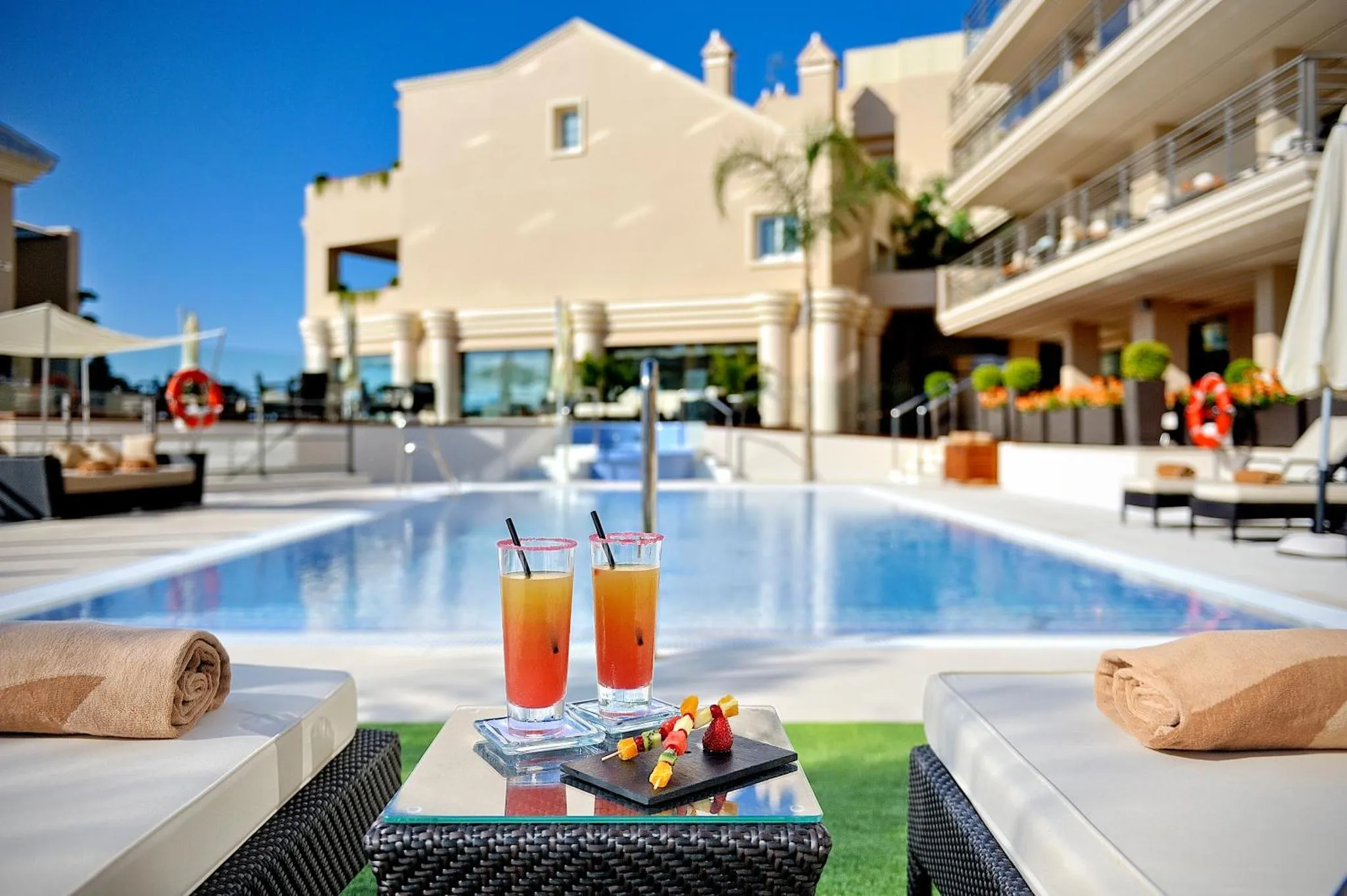 Deux verres colorés reposent sur une table basse au bord d'une piscine ensoleillée.