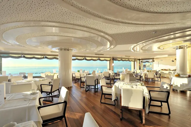 Une salle lumineuse avec des tables dressées face à une vue sur la mer.