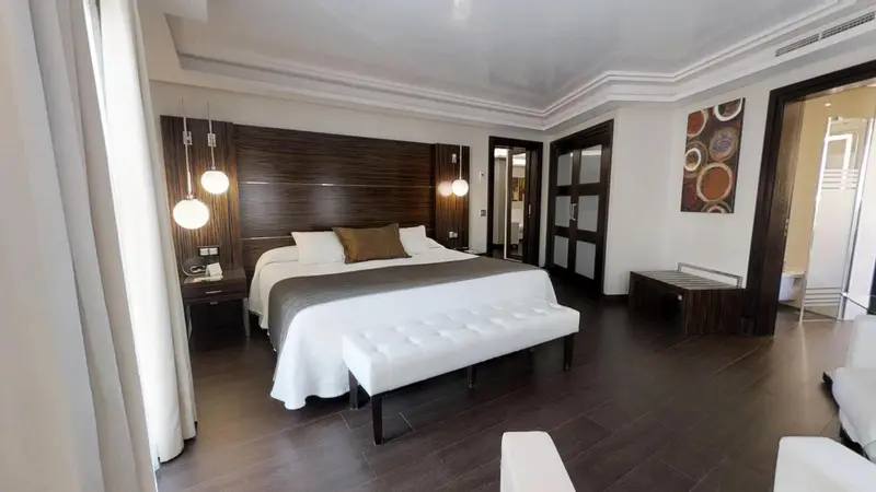 Une chambre spacieuse avec un grand lit et un banc au pied du lit.
