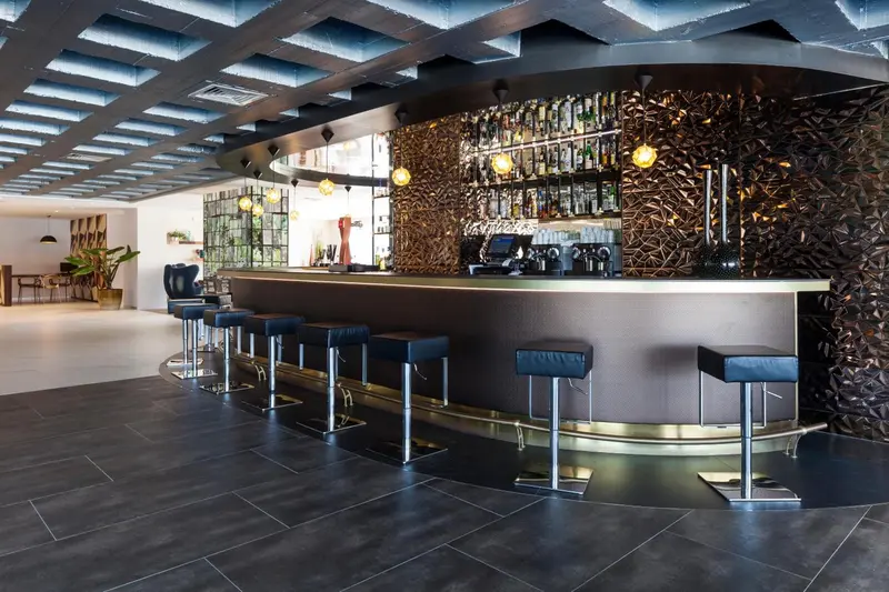 Un long comptoir de bar moderne avec des tabourets est mis en valeur par un éclairage suspendu et un mur texturé.