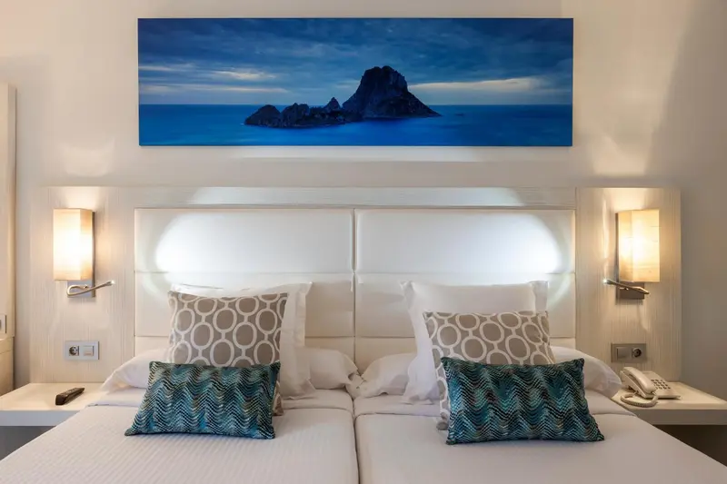 Une chambre lumineuse avec un grand lit et une vue sur une île rocheuse.