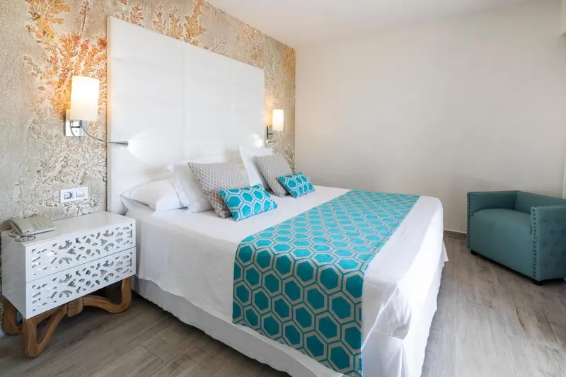 Une chambre lumineuse avec un grand lit recouvert d'une courtepointe turquoise et de coussins.