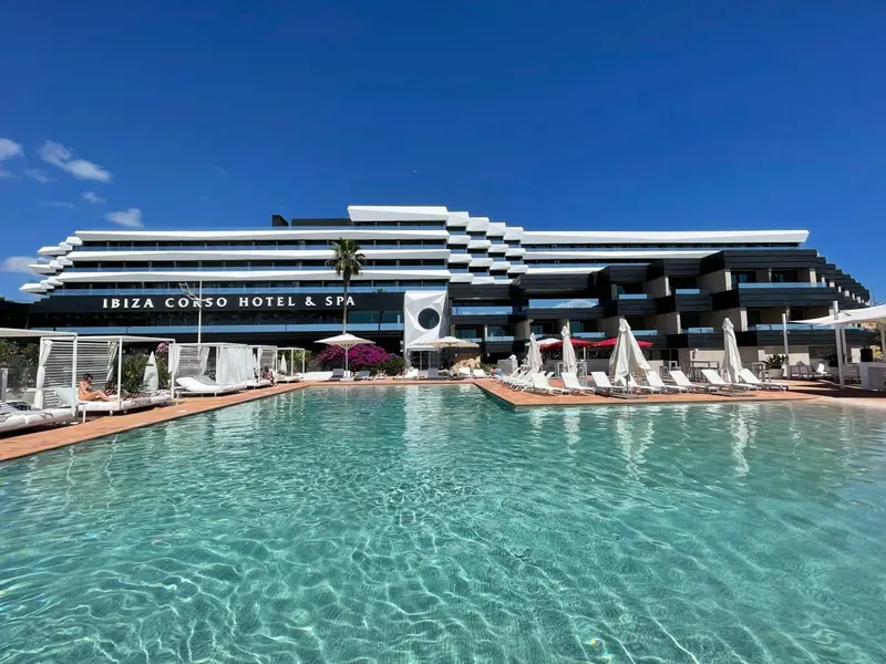 Vue d'une piscine d'hôtel avec des transats sous un ciel bleu.
