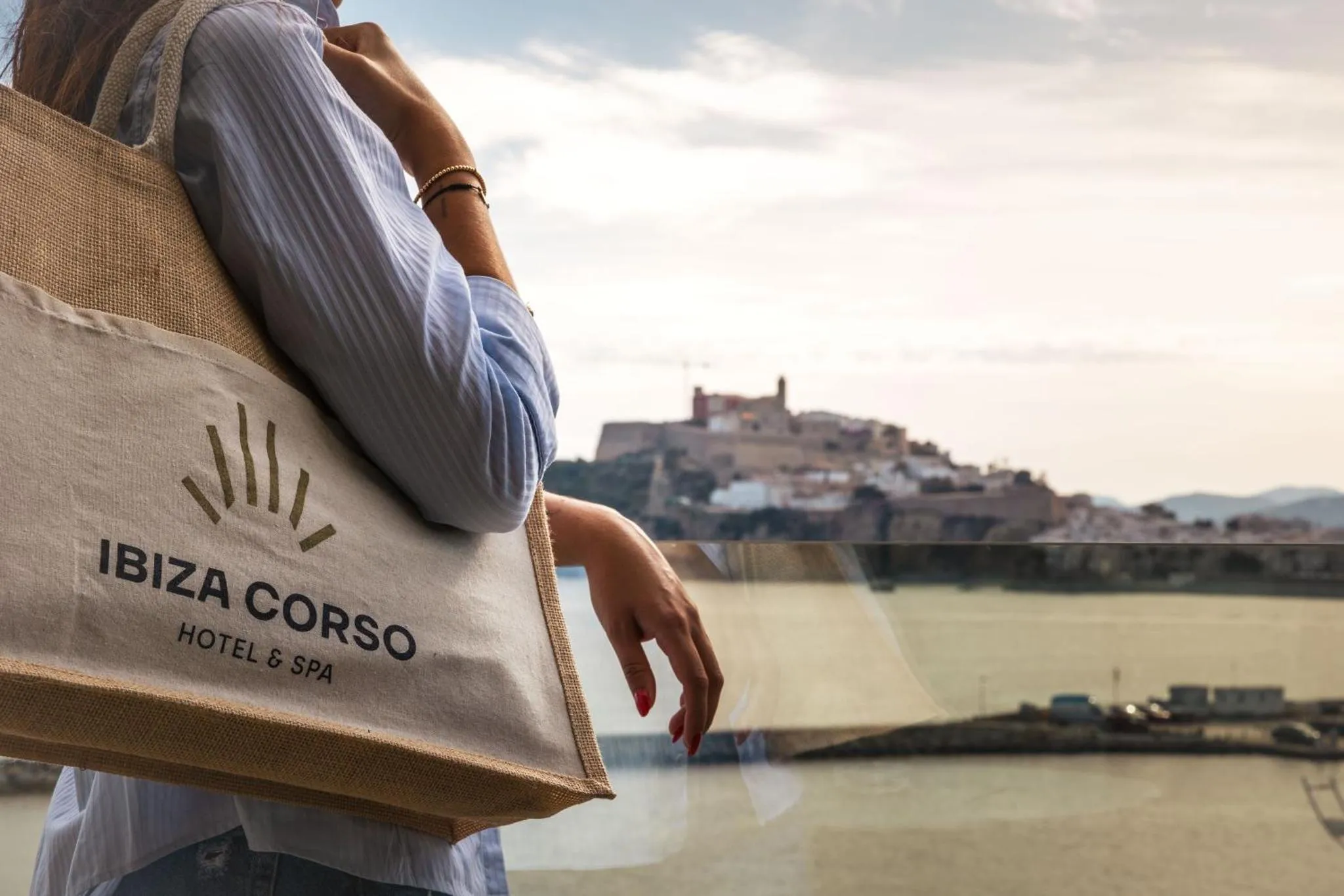 Une personne tenant un sac de toile avec une inscription devant une vue sur la mer et une ville.