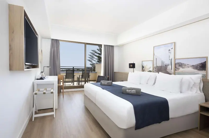 Une chambre lumineuse avec un grand lit et un balcon donnant sur la mer.