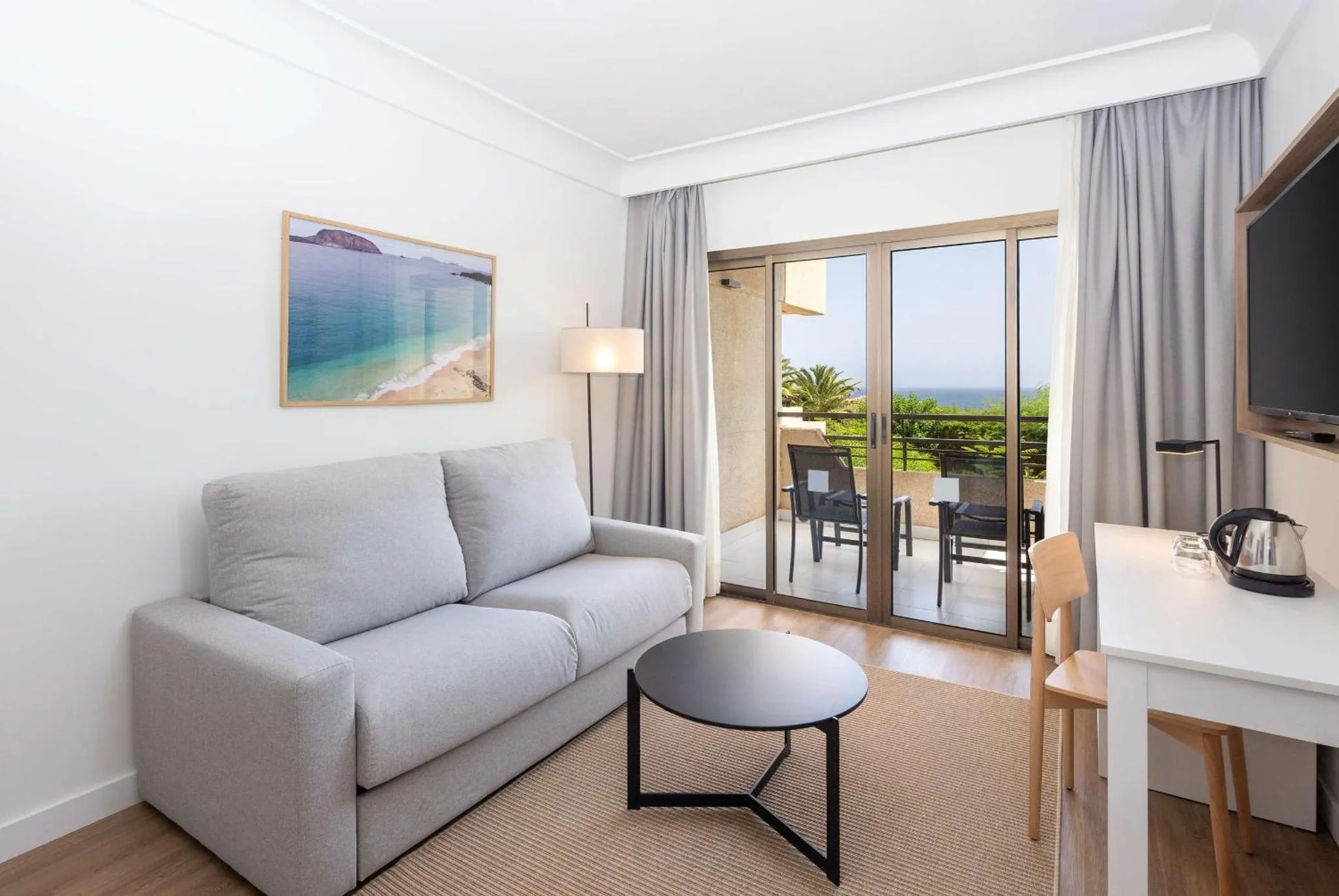 Espace de détente lumineux avec canapé et vue sur la mer depuis un balcon.