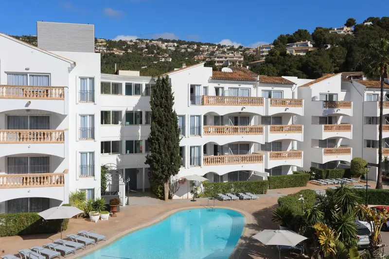 Bâtiment blanc à plusieurs étages avec des balcons et une piscine en contrebas.