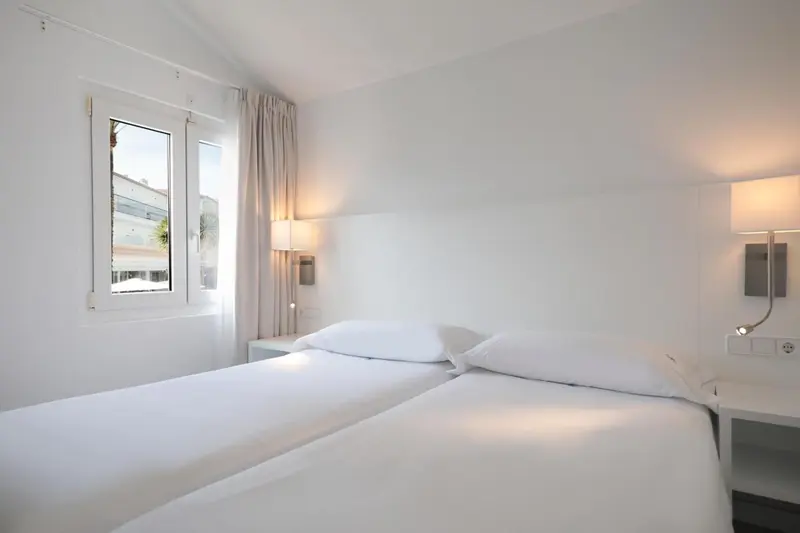 Chambre lumineuse avec deux lits simples et une fenêtre.