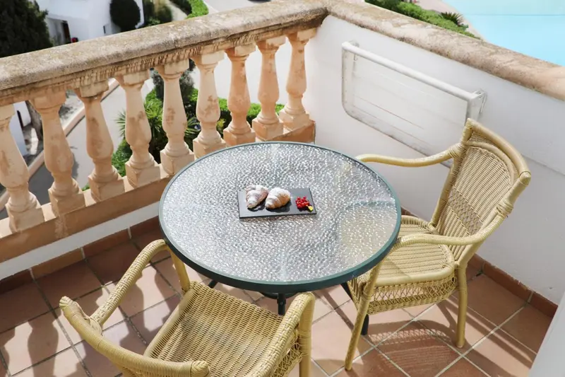 Une table ronde et deux chaises en osier sur un balcon carrelé.