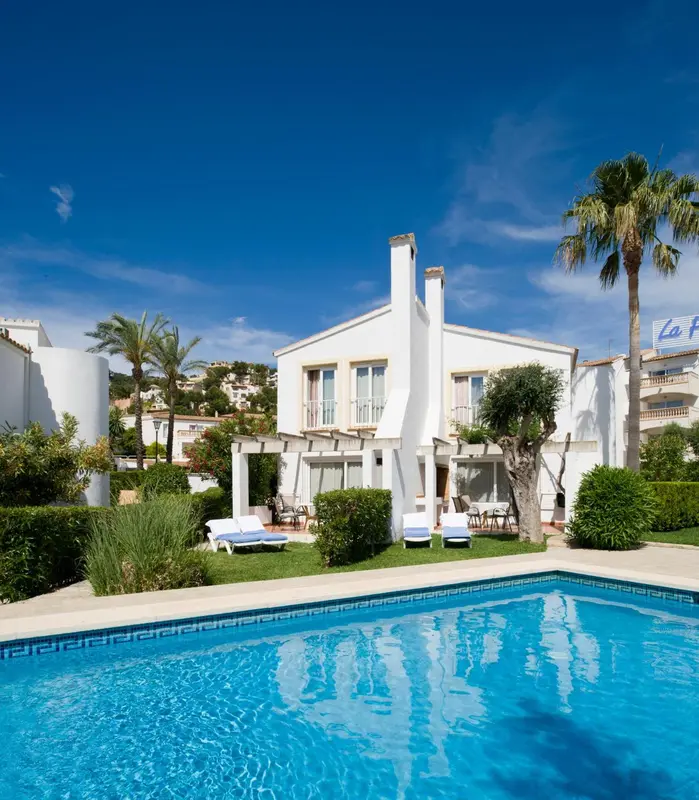 Bâtiment blanc avec piscine et végétation luxuriante sous un ciel bleu.