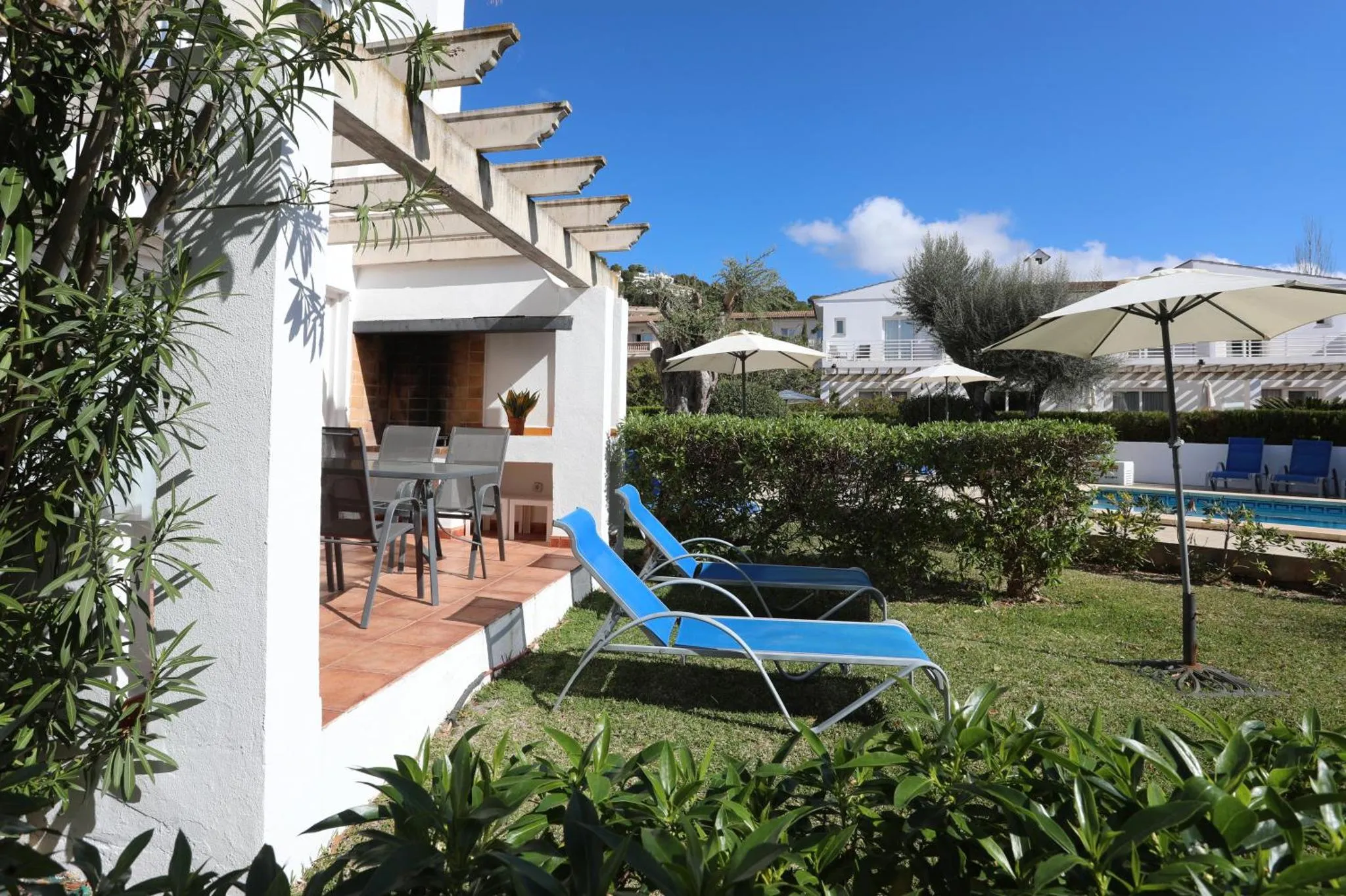 Terrasse ombragée avec mobilier de jardin et vue sur une piscine.