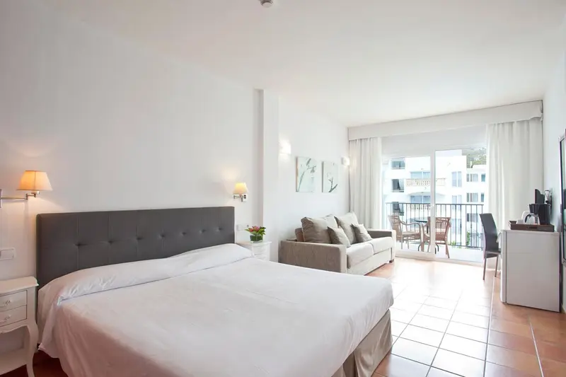 Une chambre lumineuse avec un grand lit et un coin salon donnant sur une terrasse.