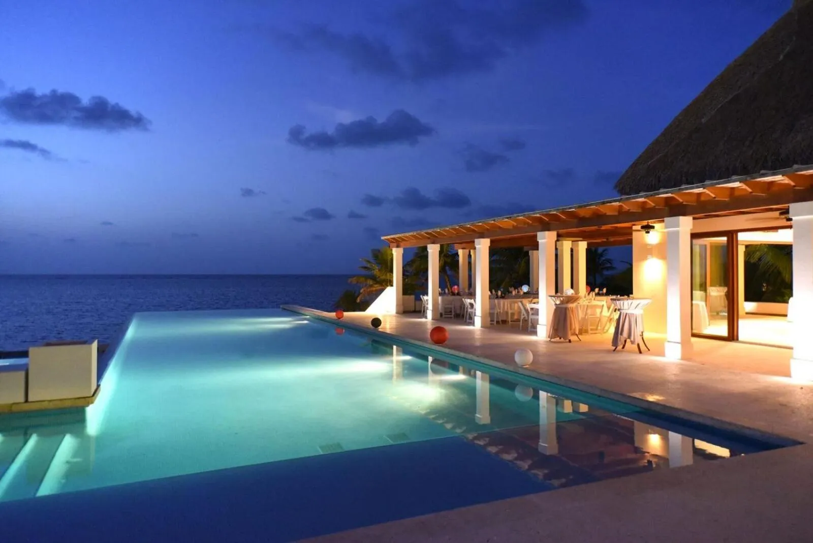 Piscine illuminée avec vue sur la mer au crépuscule.