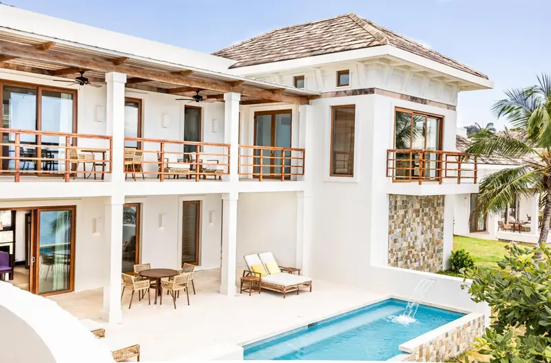 Bâtiment blanc à deux étages avec des balcons et une petite piscine.