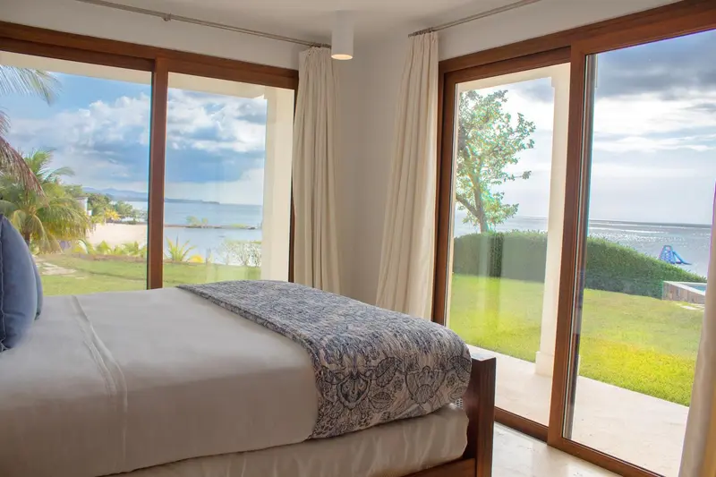 Une chambre lumineuse avec un grand lit face à une baie vitrée donnant sur la mer.