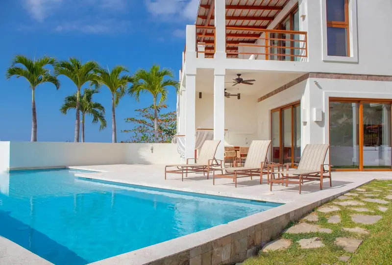 Transats et petite piscine devant un bâtiment blanc avec des palmiers.
