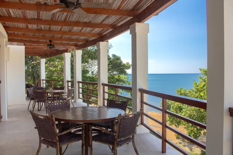 Terrasse ombragée avec tables et chaises donnant sur la mer.