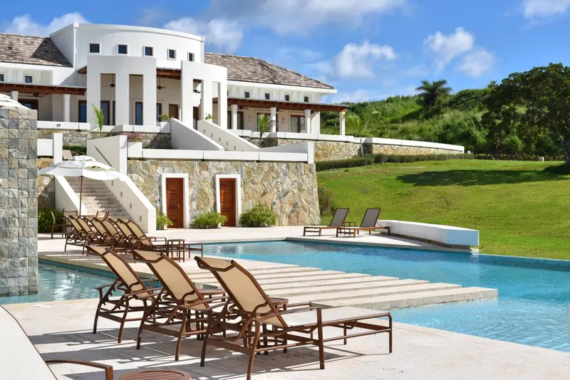 Transats alignés au bord d'une piscine devant un bâtiment blanc.