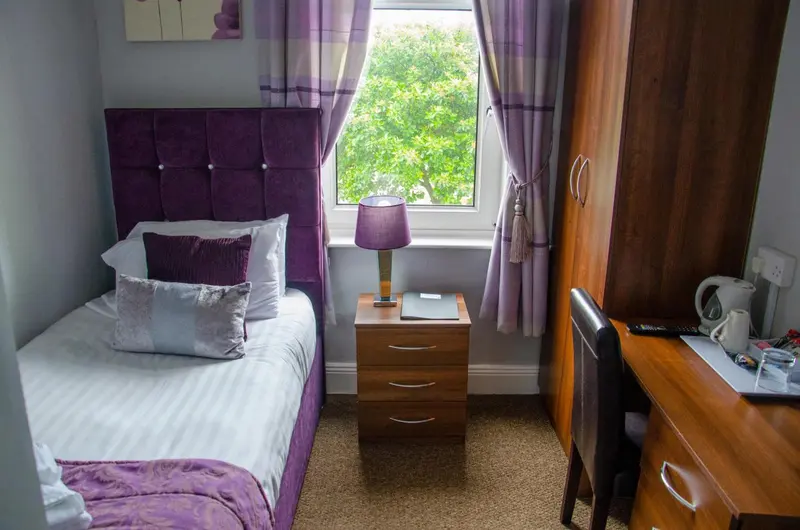Une chambre avec un lit simple et un bureau près d'une fenêtre.