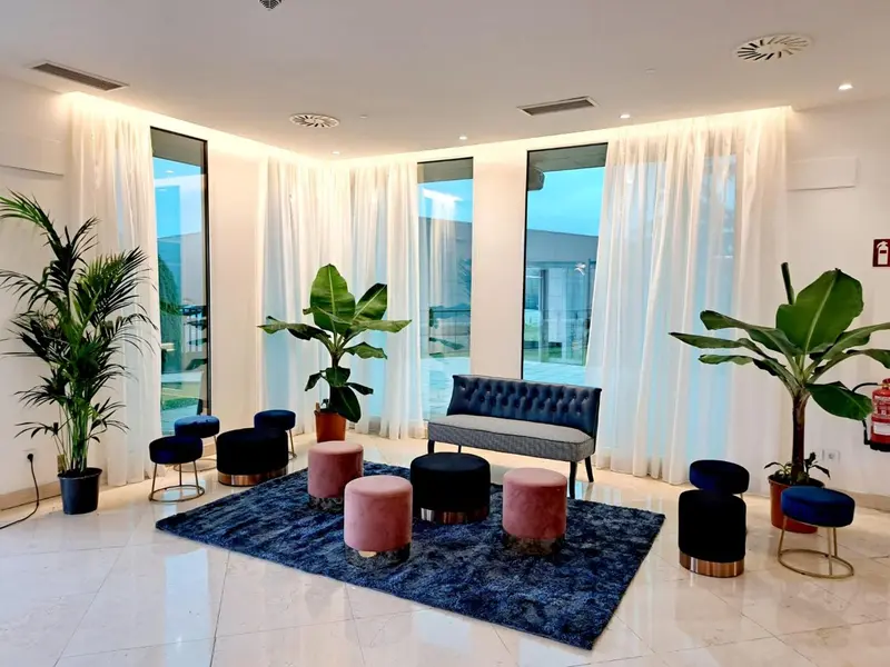 Espace de détente lumineux avec canapés et plantes vertes près de grandes fenêtres.