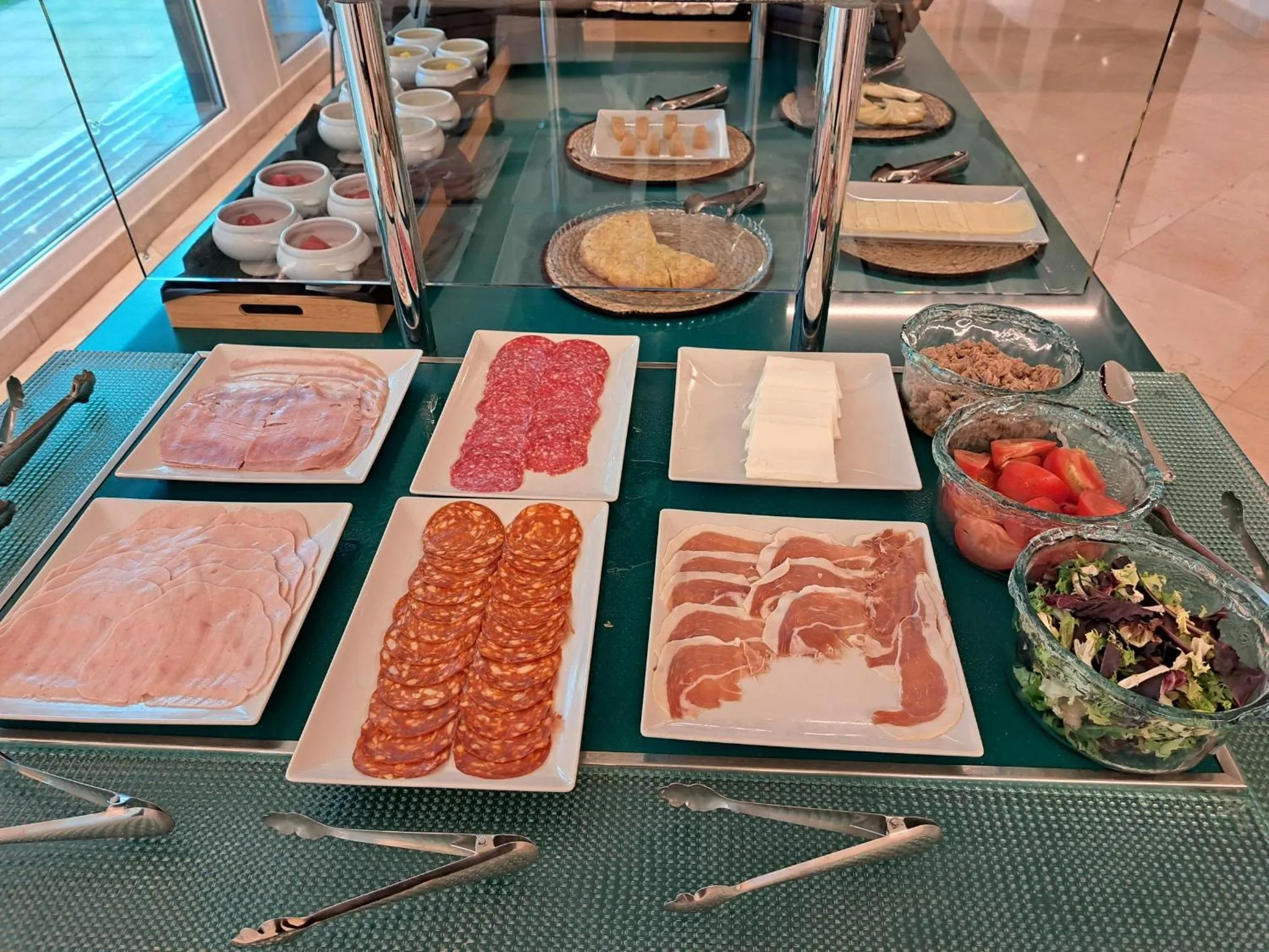 Présentation de charcuteries, fromages et salades sur un buffet.