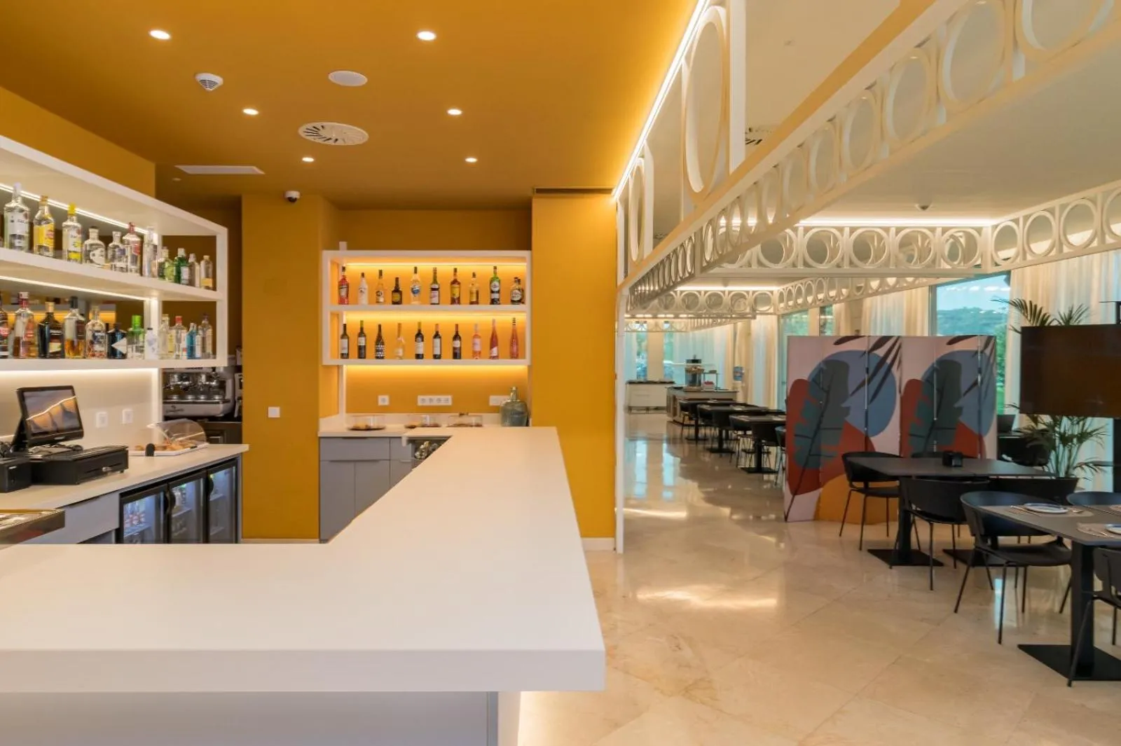 Un comptoir de bar moderne avec des étagères remplies de bouteilles, dans un espace lumineux et coloré.