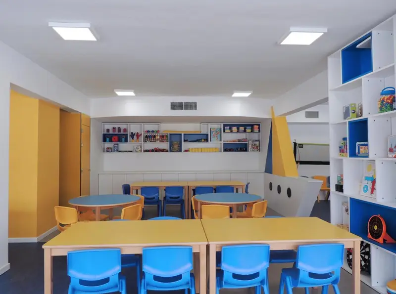 Une salle lumineuse avec des tables et des chaises colorées, des étagères remplies de jeux et de livres.