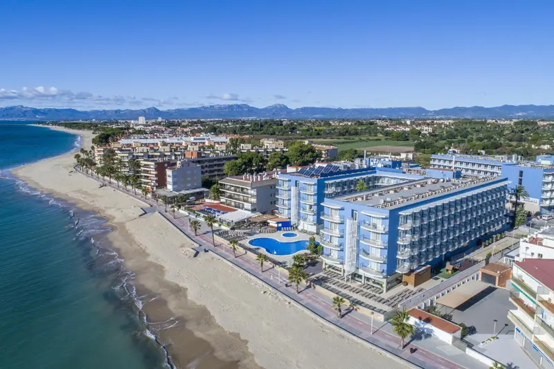 Vue aérienne d'un complexe hôtelier blanc et bleu bordant une plage de sable fin.