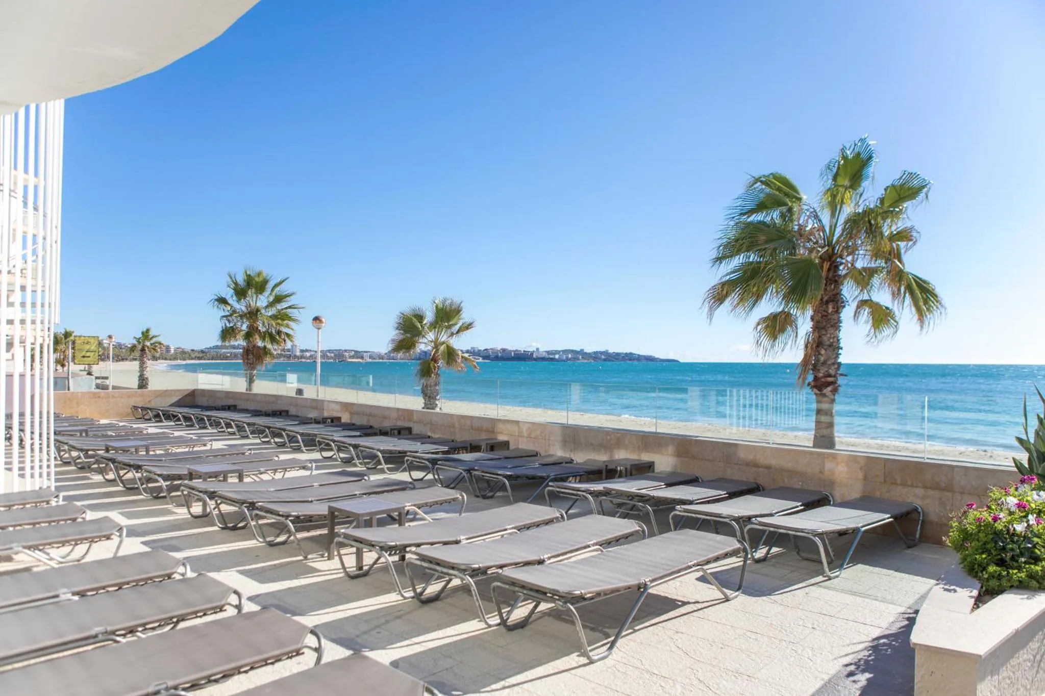 Transats alignés sur une terrasse ensoleillée face à la mer.