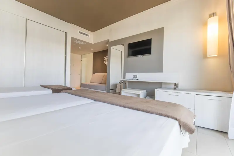 Une chambre lumineuse avec deux lits simples et un téléviseur mural.