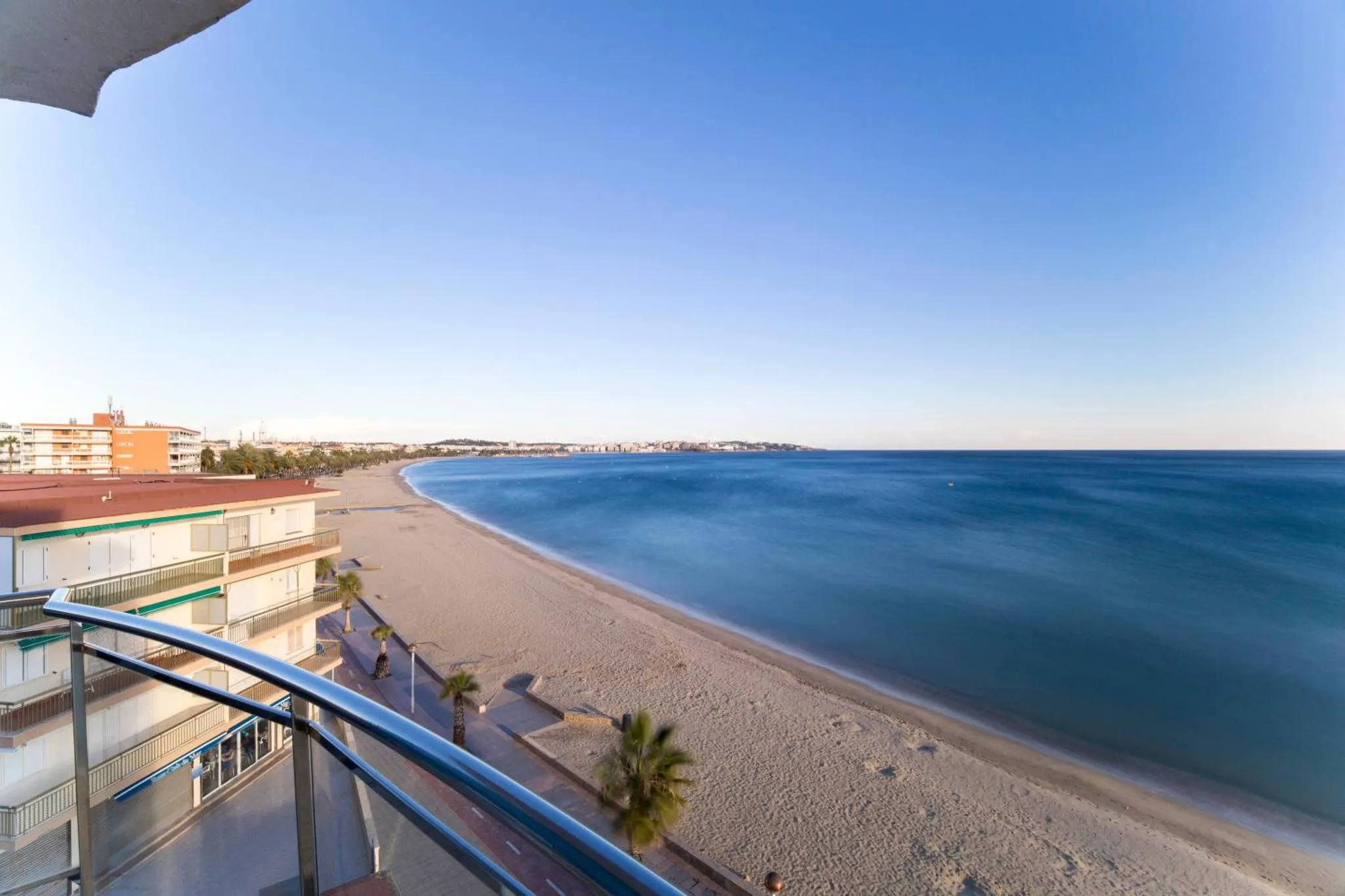 Vue d'une plage de sable fin et d'une promenade en bord de mer depuis un balcon.