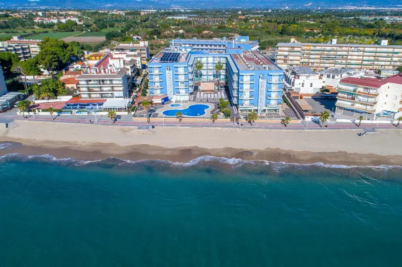 Vue aérienne d'un complexe hôtelier bleu et blanc bordant une plage de sable fin.