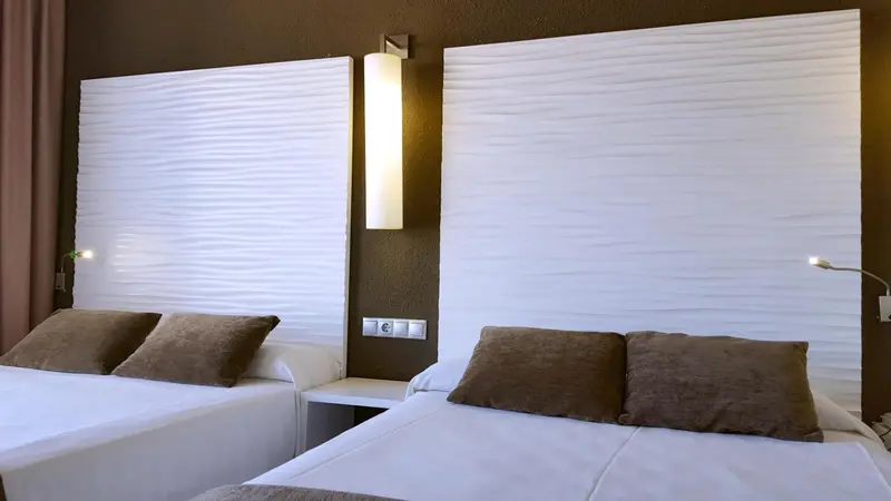 Deux lits simples avec des têtes de lit blanches et des oreillers marron dans une chambre.