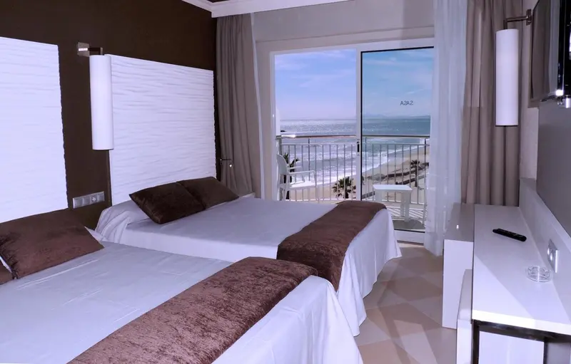 Chambre lumineuse avec lits jumeaux et vue sur la mer.