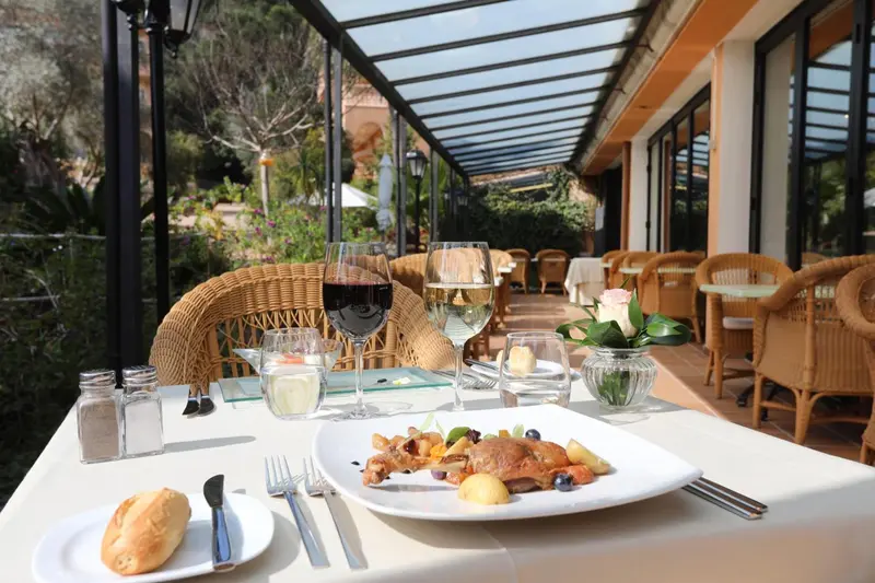 Une table est dressée avec des plats et des boissons sur une terrasse ombragée.