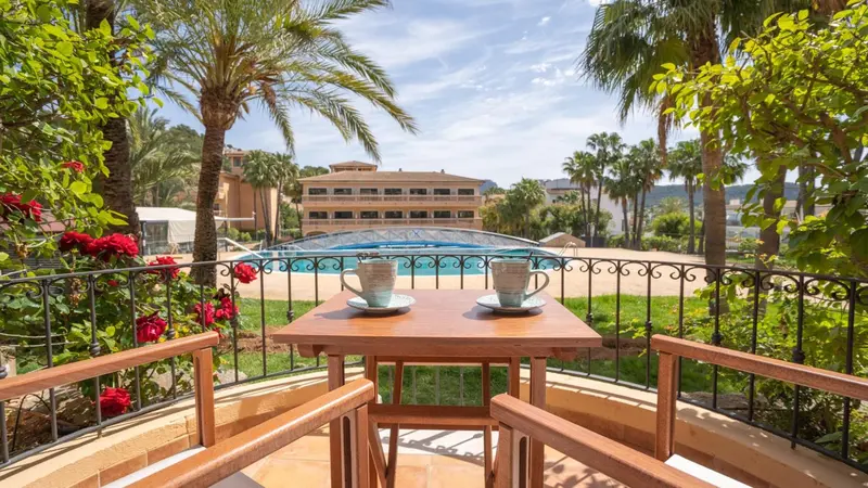 Une table avec deux tasses sur un balcon fleuri donne sur une piscine et une végétation luxuriante.