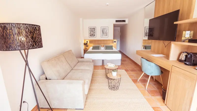 Une chambre lumineuse avec un canapé, un bureau et un grand téléviseur mural.