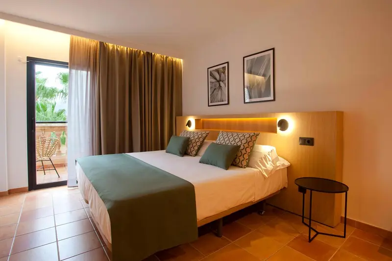 Chambre lumineuse avec un grand lit et un accès à une terrasse.